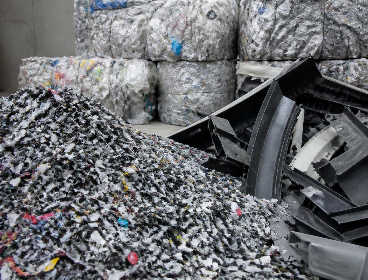 Fardos de plástico, flocos de plástico triturado e recortes de compósitos numa nave industrial